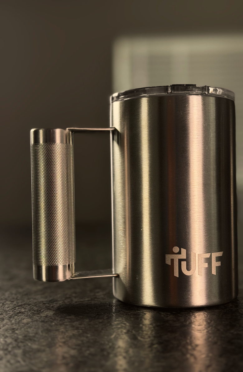 The silver Tuff Mug standing on a dark kitchen counter, lid seated, knurled barbell handle to the left.
