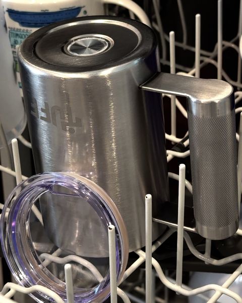 The silver Tuff Mug lying in a loaded dishwasher rack with its lid ring beside it.